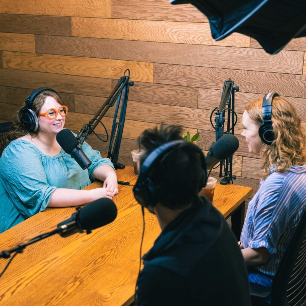 Three people in the studio seated around a table with headphones and microphones