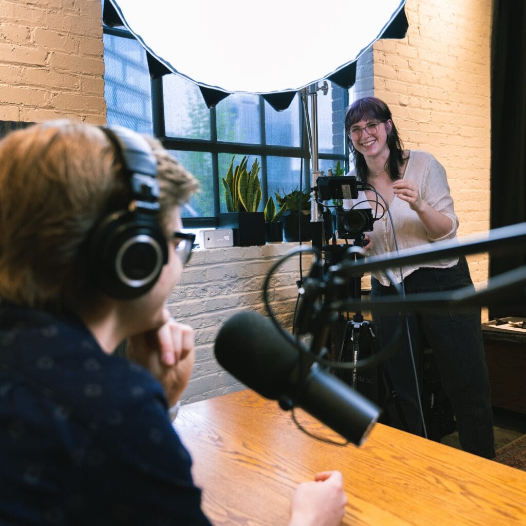 Women video recording man with headphones and mic in studio with large softbox key light 