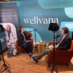 Man interviewing a woman in the trade show booth with studio lights, headphones, and large microphones